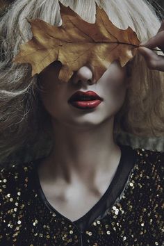 a woman with blond hair and red lipstick holding a leaf over her face