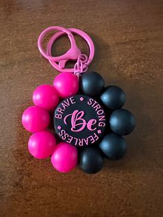 a pink and black keychain that has some balls around it on a table