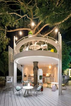 an outdoor dining area is lit up at night with lights shining on the trees and furniture