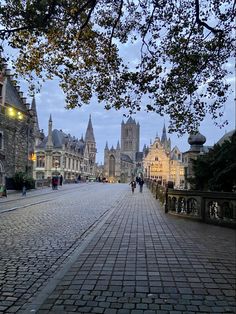 a cobblestone street with people walking on the sidewalk and buildings in the background