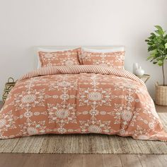 a bed with an orange and white flowered comforter on it, next to a potted plant