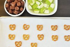 pretzels and apples are arranged on a baking sheet next to bowls of candy