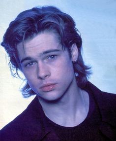 a young man with long hair wearing a black shirt and earrings looking at the camera