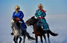 two women riding horses in the snow on a sunny day with blue sky behind them