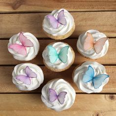 six cupcakes with white frosting and colorful butterflies on them sitting on a wooden table