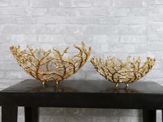 two decorative gold corals sitting on top of a black table next to a brick wall