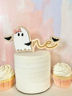 two cupcakes are sitting next to a cake with a ghost decoration on top