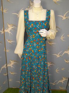 "Fabulous floral maxi dress dating 1970s. Made from a floral cotton fabric, it has a design of red and yellow flowers on a blue background.  Designed to look like a pinafore dress worn over a blouse, it has contrasting ivory crepe sleeves and bib insert, with a high neckline, and pintucked and button details. The sleeves are gathered at the shoulder, with elasticated cuffs. It fastens at the back with a zip, and has a half belt which ties at the back. Labelled size 38, would fit a current UK 10. Measures 36\" bust, 29\" waist.  Length 52.5\" from shoulder to hem. Measures 14\" across the shoulders. In excellent vintage condition." Vintage Square Neck Maxi Dress For Garden Party, 1970s Style Blue Floral Print Dresses, Spring Vintage Maxi Dress With Square Neck, Vintage Square Neck Maxi Dress For Spring, Blue Sleeveless Vintage Maxi Dress, Vintage Blue Dress With Ditsy Floral Print, Vintage Blue Maxi Dress For Garden Party, Blue Vintage Maxi Dress For Garden Party, Vintage Blue Maxi Dress