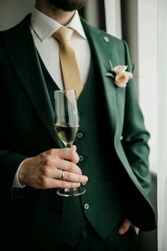 a man in a green suit holding a wine glass with a flower on his lapel