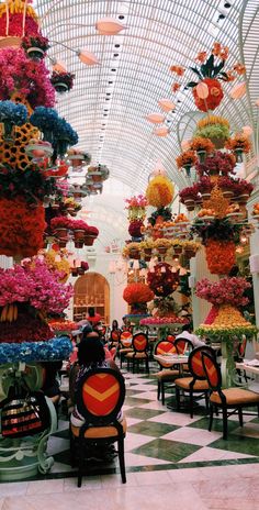 the inside of a flower shop with lots of flowers hanging from the ceiling and chairs