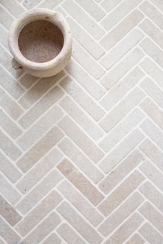 a white vase sitting on top of a floor next to a tiled flooring pattern