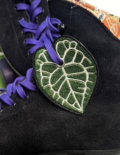 a pair of black boots with purple laces and a green leaf on the sole