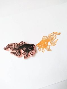 two goldfish brooches sitting next to each other on top of a white surface