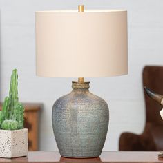 a table lamp sitting on top of a wooden table next to a potted cactus