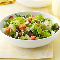 a white bowl filled with salad sitting on top of a yellow tablecloth covered table