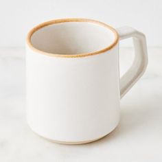 a white coffee mug sitting on top of a marble counter next to a wooden spoon