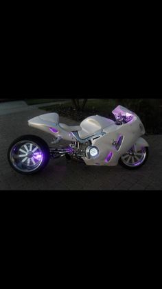 a white motorcycle with purple lights on the front wheel and side view mirror behind it