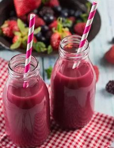 two glasses filled with red smoothie next to strawberries on a checkered table cloth