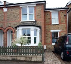 a car is parked in front of a brick house with white windows and shutters