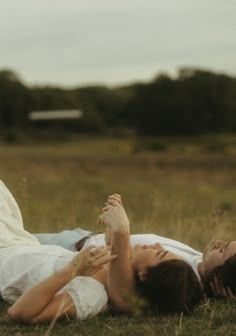 two women laying on the ground in a field with one holding her hand up to her head