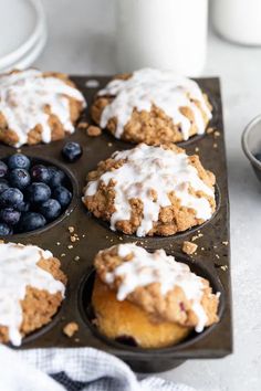 muffins with icing and blueberries in a muffin tin on a table