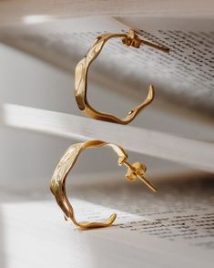 two pairs of gold - plated metal hoop earrings on top of an open book