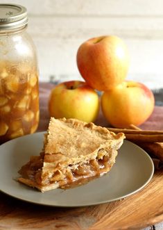 a slice of apple pie on a plate next to apples and cinnamon sticks in a jar