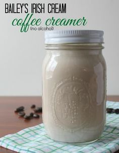 a glass jar filled with coffee creamer sitting on top of a table next to beans