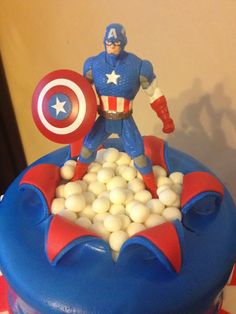 a captain america cake with white balls in the shape of a rocket ship and an action figure on top