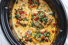 a crock pot filled with chicken and spinach covered in cheese, sauce and tomatoes