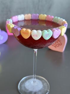 a heart - shaped drink in a martini glass with conversation hearts on the rims