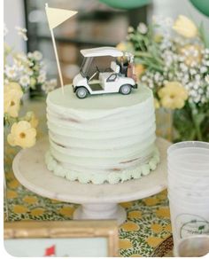 a wedding cake with a car on top and flowers in vases behind the cake