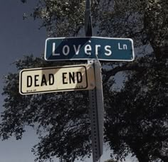 two street signs that are on top of a sign post with trees in the background