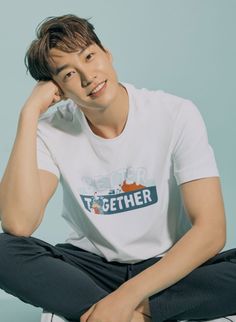 a young man sitting on the ground wearing a white t - shirt