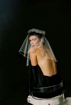 a woman wearing a veil sitting on top of a white bucket with her back to the camera