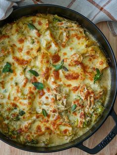 a casserole dish with cheese and spinach in a black pan on a wooden table