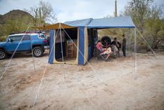 two people sitting in chairs under a tent on the side of a dirt road next to a blue truck