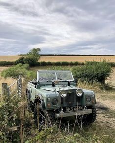 an old green jeep is parked on the side of a dirt road near a field