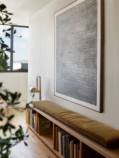 a large painting hangs on the wall next to a bench and bookshelf filled with books