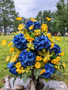 a vase filled with blue and yellow flowers sitting on top of a stone slab in the grass