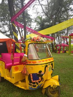 a yellow tuk - tuk parked in the grass with pink and yellow decorations