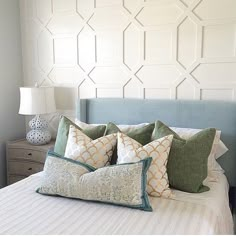 a bed with several pillows on top of it and a lamp next to the headboard