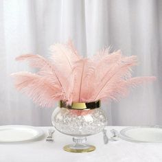 there is a vase with some feathers in it on top of a white table cloth