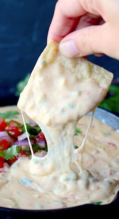 a hand dipping tortilla chips into a bowl of dip