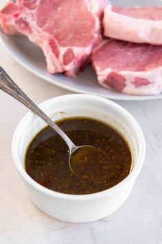 a bowl of sauce next to some meat on a white plate with a spoon in it