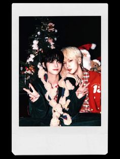 two people posing for a photo in front of a christmas tree with santa hats on