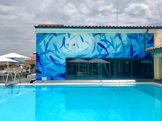 an empty swimming pool in front of a building with a painted mural on it's side