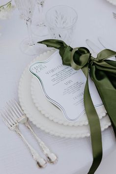 the table is set with white plates and silverware, green satin ribbon on each plate