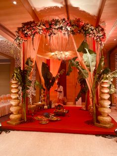 a mandap decorated with flowers and greenery on a red carpeted floor