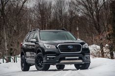 the front end of a black subarunt parked on a snow covered road with trees in the background